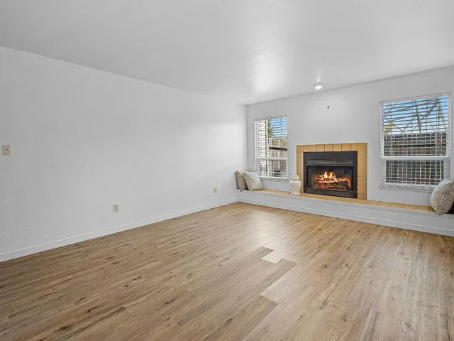 an empty room with wooden floor fire place and windows