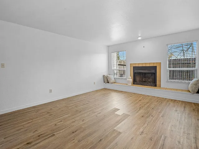 an empty room with wooden floor fireplace and windows