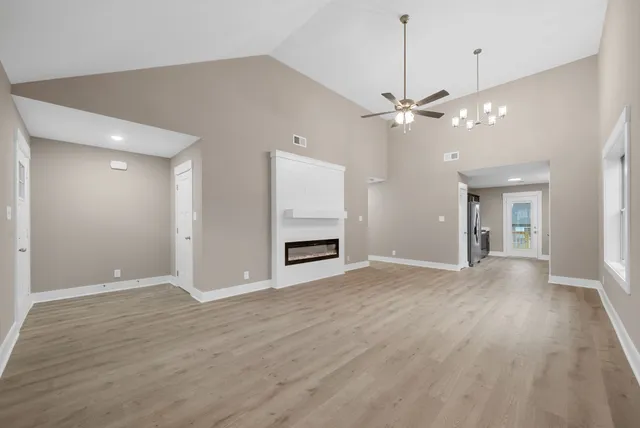 an empty room with wooden floor chandelier and windows