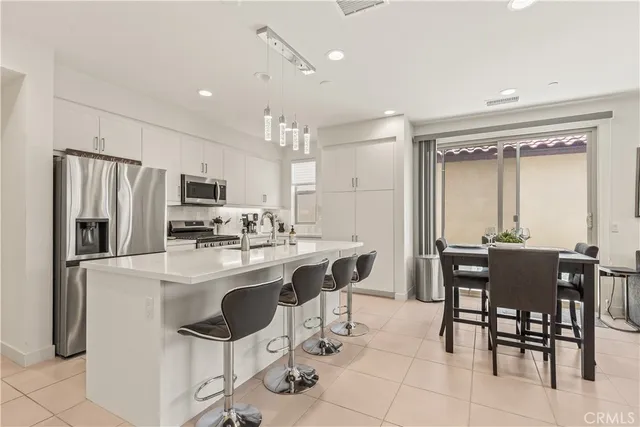 a kitchen with stainless steel appliances a dining table chairs refrigerator and sink