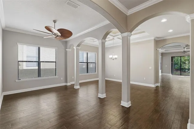 an empty room with wooden floor chandelier fan and windows