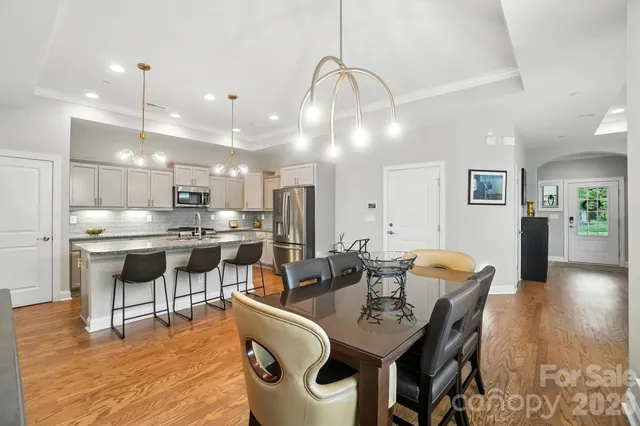 a kitchen with stainless steel appliances kitchen island granite countertop a sink a stove a dining table and chairs with wooden floor