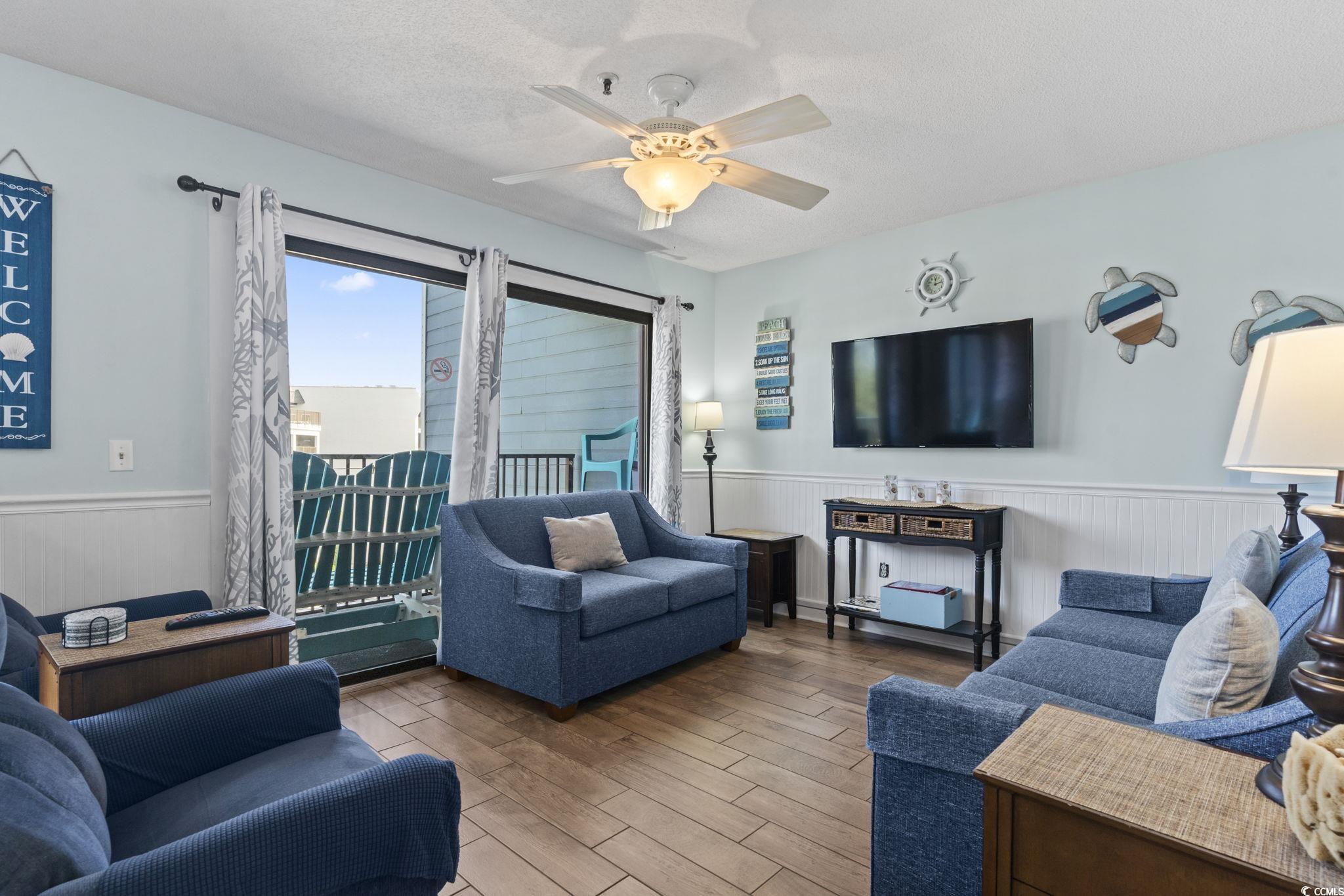 5905 South Kings Highway, Unit 451B Myrtle Beach, SC 29575 - Photo 4 of 37 Living room with a textured ceiling, a wainscoted wall, wood finished floors, and ceiling fan