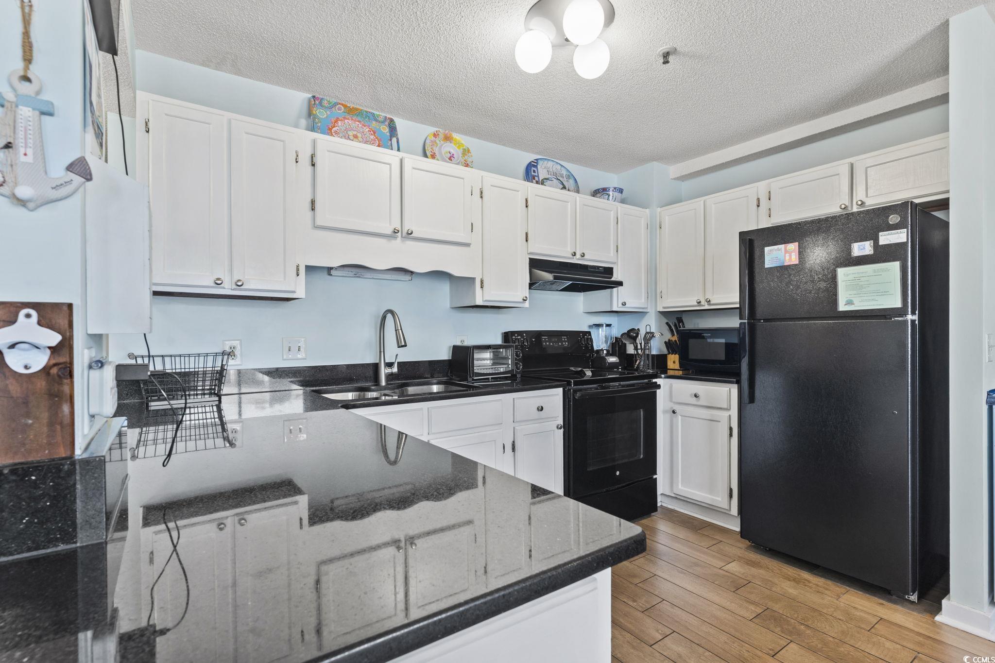 5905 South Kings Highway, Unit 451B Myrtle Beach, SC 29575 - Photo 8 of 37 Kitchen with white cabinets, black appliances, light wood-style flooring, dark stone counters, and a textured ceiling