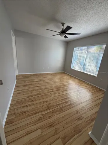 an empty room with wooden floor fan and windows