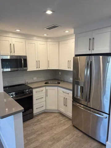 a kitchen with stainless steel appliances granite countertop a refrigerator a stove a sink and white cabinets