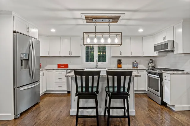 a kitchen with stainless steel appliances granite countertop a stove a refrigerator a sink dishwasher a dining table and chairs with wooden floor
