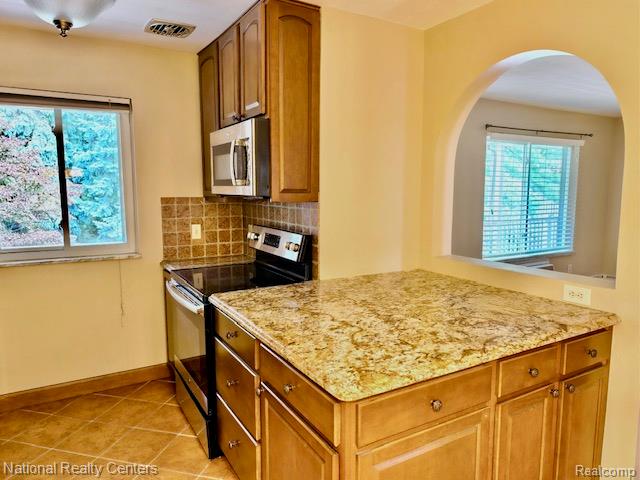 475 South Adams Road, Unit 19 Birmingham, MI 48009 - Photo 9 of 20 Kitchen featuring an arched pass-through, wood-finish cabinetry, stainless steel appliances, granite countertops, and tile flooring