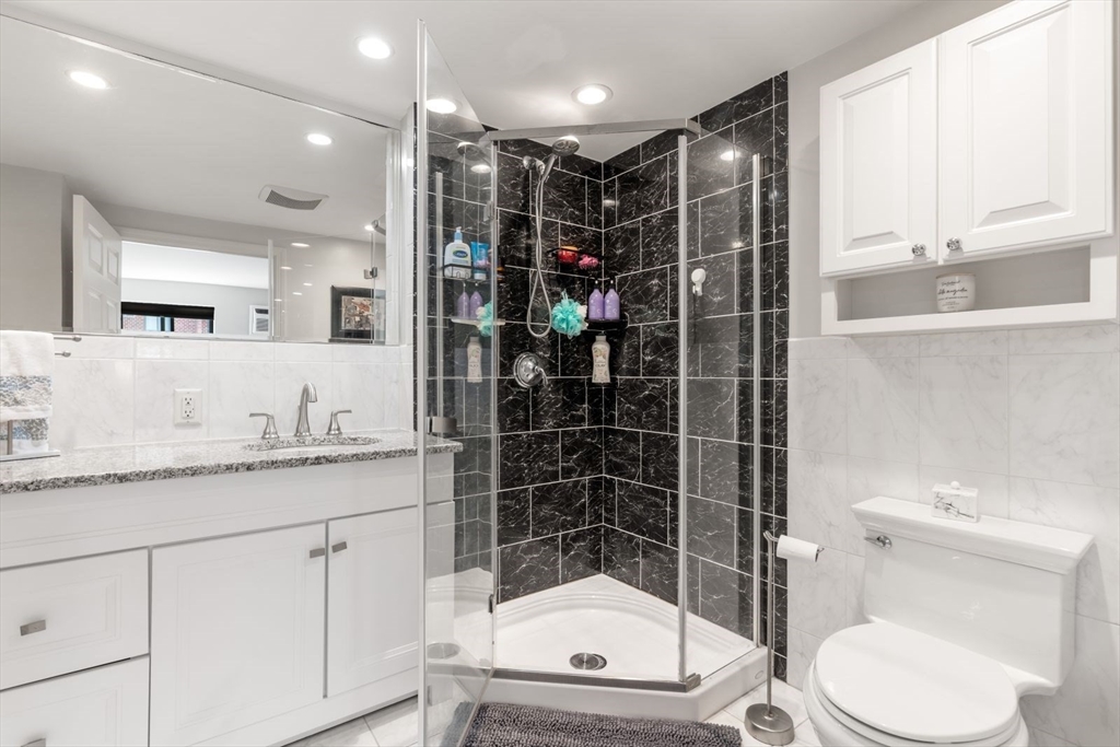 135 Franklin Street, Unit 101 Stoneham, MA 02180 - Photo 13 of 24 a bathroom with a granite countertop sink toilet a mirror a vanity and shower