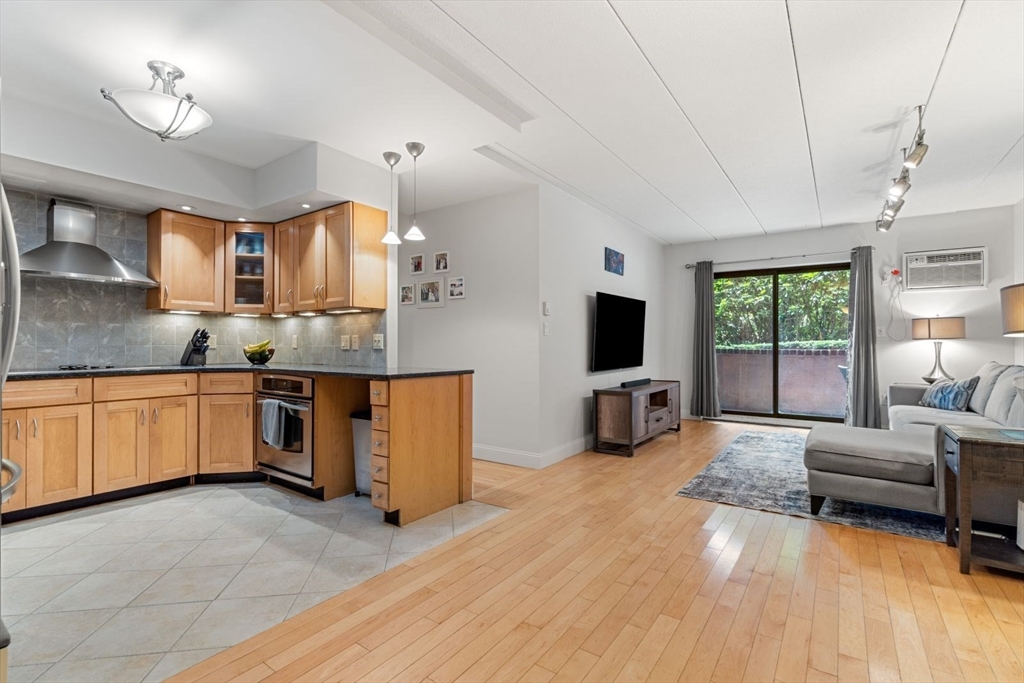 135 Franklin Street, Unit 101 Stoneham, MA 02180 - Photo 4 of 24 a large living room with stainless steel appliances granite countertop a stove a sink dishwasher a flat tv screen and a dining table with wooden floor