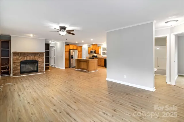 an empty room with wooden floor fireplace and a kitchen view