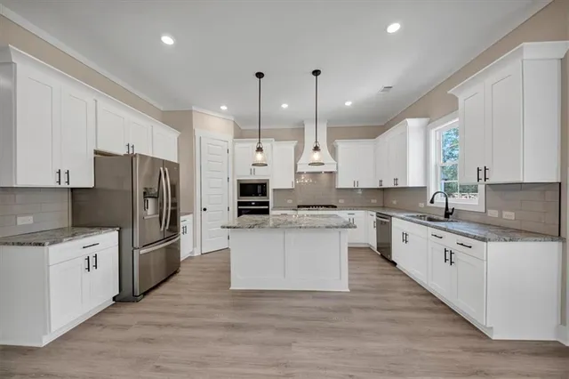 a kitchen with stainless steel appliances granite countertop a refrigerator a sink dishwasher a stove and white cabinets with wooden floor