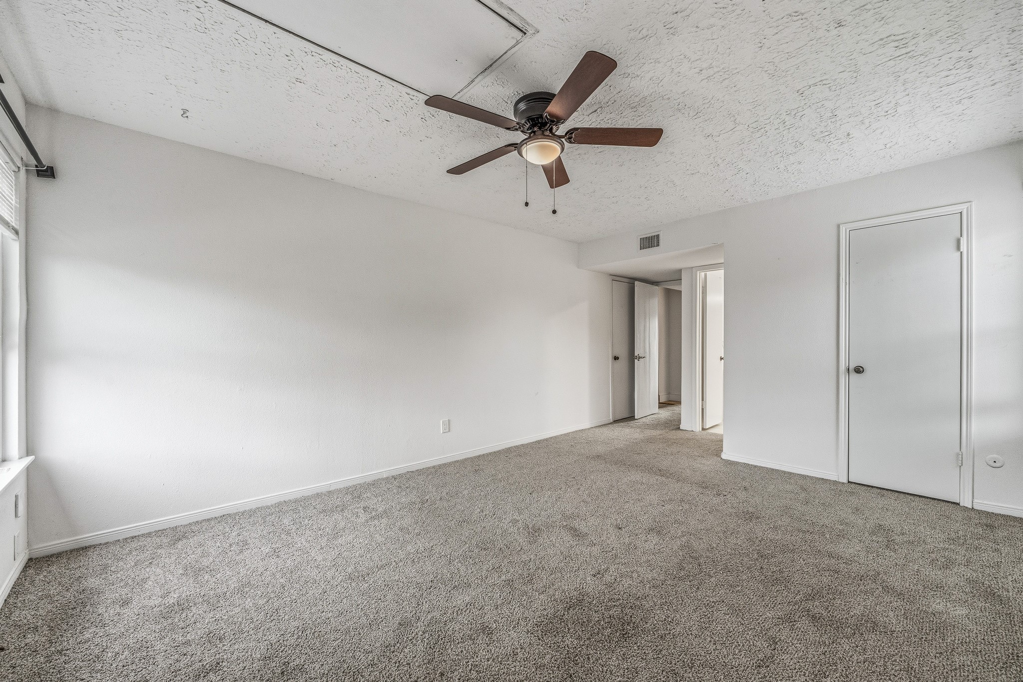 830 Threadneedle Street, Unit 240 Houston, TX 77079 - Photo 19 of 33 This room features neutral carpeting, white textured walls, and a ceiling fan. It's well-lit with natural light from a window and includes two doors, offering potential for storage or access to other areas.