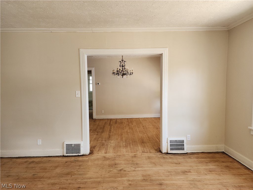 3566 Daleford Road Cleveland, OH 44120 - Photo 9 of 15 Spare room with ornamental molding, a textured ceiling, a notable chandelier, and light hardwood / wood-style floors