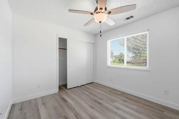 an empty room with wooden floor ceiling fan and windows