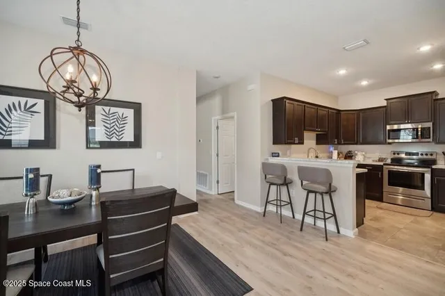 a open dining room with wooden floor a chandelier a wooden table and chairs