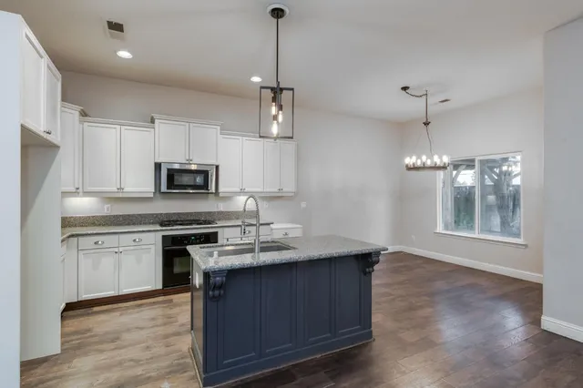 a kitchen with stainless steel appliances granite countertop a sink a stove a refrigerator cabinets and wooden floor