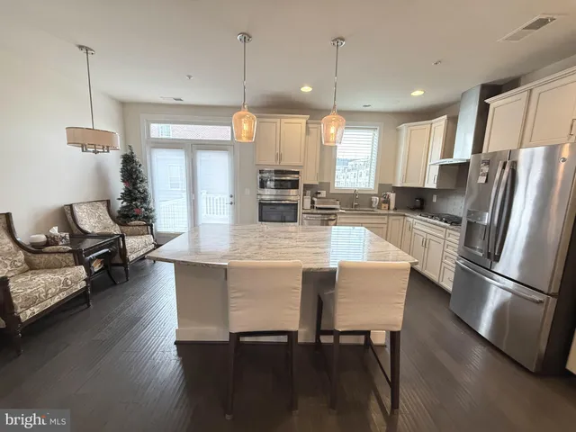 a kitchen with stainless steel appliances granite countertop a stove refrigerator a dining table and chairs with wooden floor