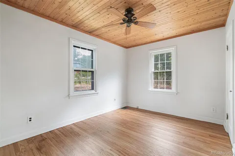 an empty room with wooden floor chandelier fan and windows