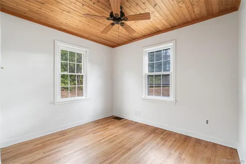 an empty room with wooden floor ceiling fan and windows