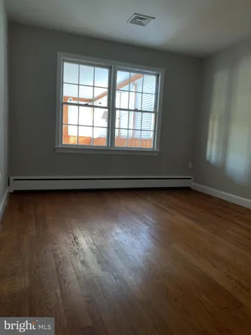 an empty room with wooden floor and windows with curtains