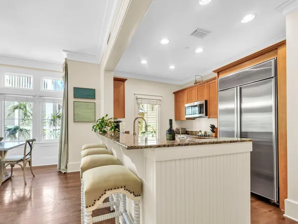 a living room with stainless steel appliances kitchen island granite countertop a refrigerator a sink dishwasher a dining table and chairs with wooden floor