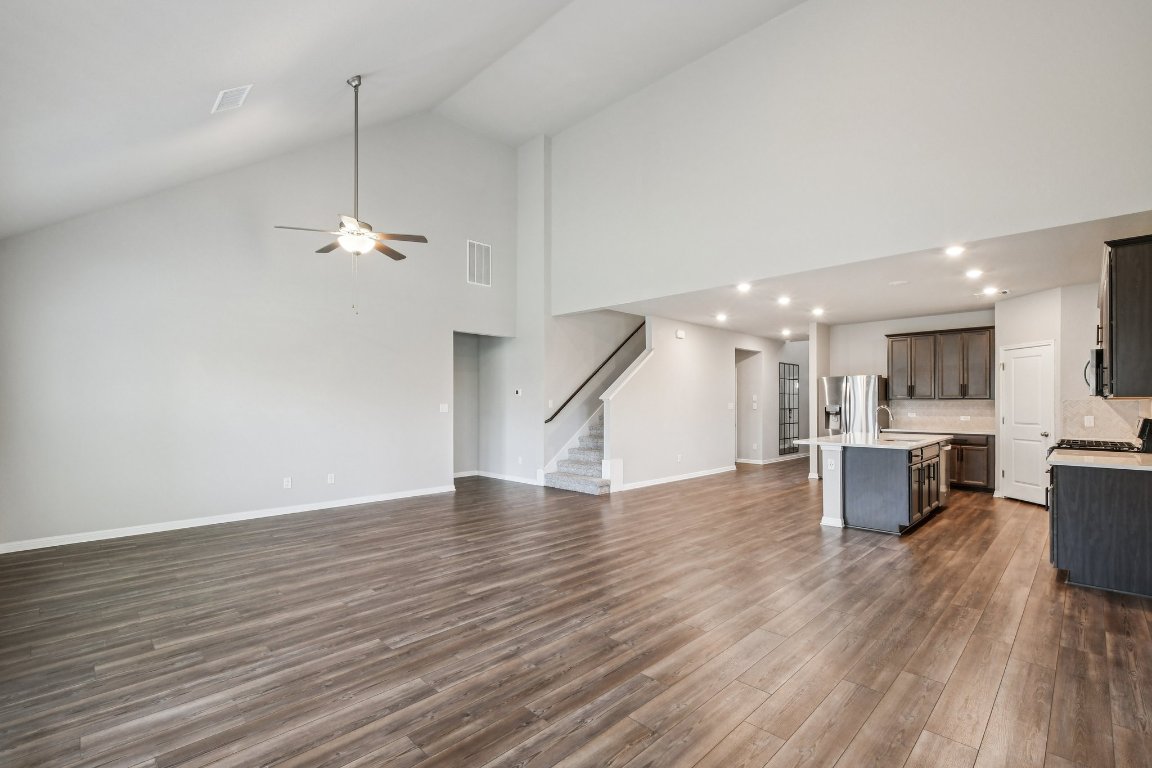 1007 Guadalupe Bass Road Hutto, TX 78634 - Photo 8 of 39 Unfurnished living room featuring dark wood-type flooring, high vaulted ceiling, ceiling fan, and stairway