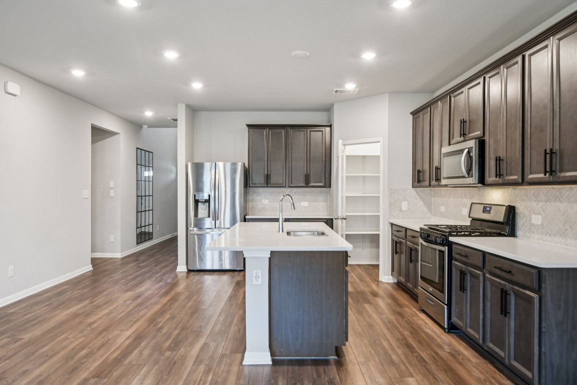 1007 Guadalupe Bass Road Hutto, TX 78634 - Photo 9 of 39 Kitchen with stainless steel appliances, an island with sink, dark brown cabinetry, backsplash, and recessed lighting