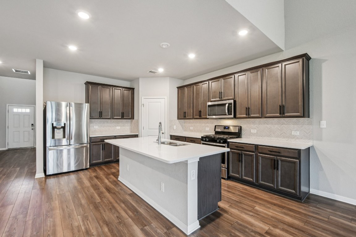 1007 Guadalupe Bass Road Hutto, TX 78634 - Photo 10 of 39 Kitchen with decorative backsplash, dark brown cabinetry, stainless steel appliances, a kitchen island with sink, and recessed lighting