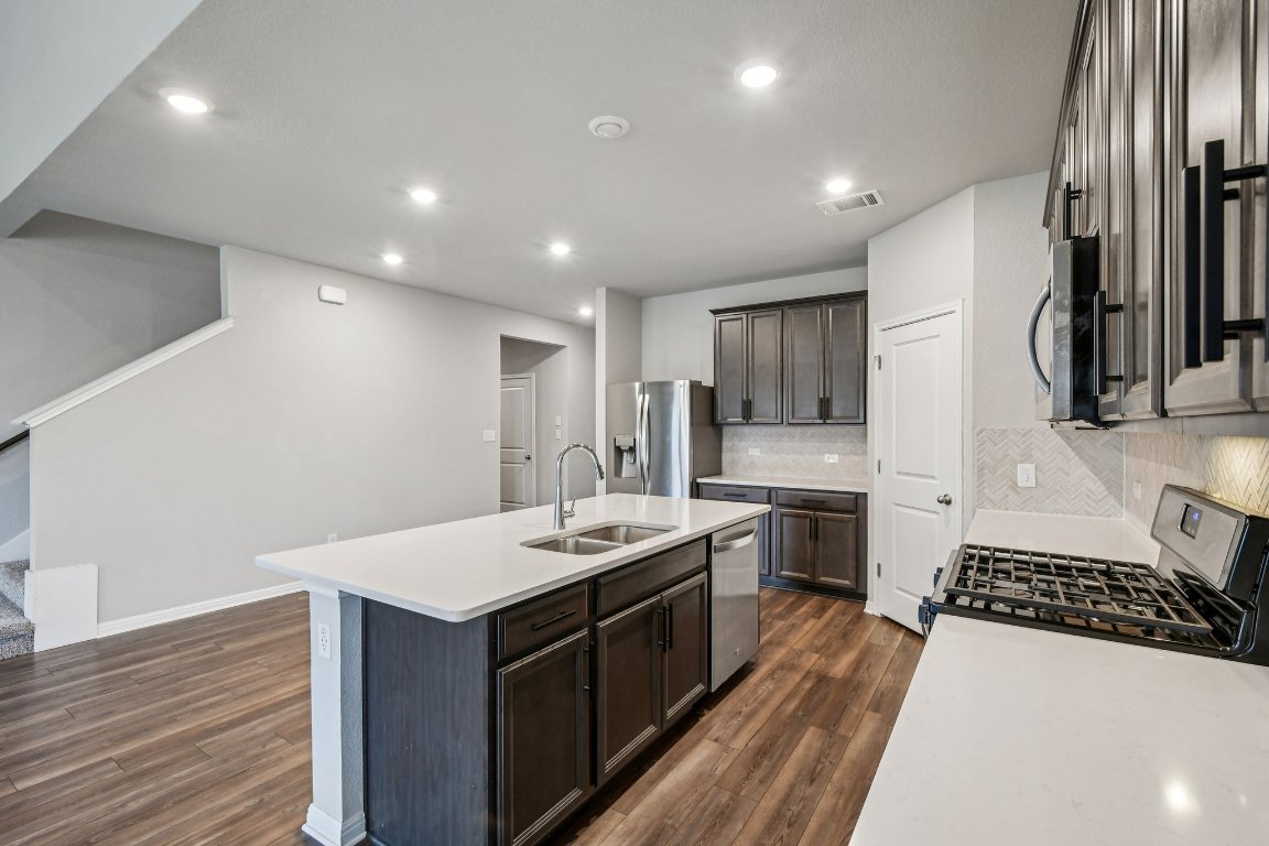 1007 Guadalupe Bass Road Hutto, TX 78634 - Photo 11 of 39 Kitchen featuring tasteful backsplash, a center island with sink, stainless steel appliances, dark brown cabinets, and dark wood-style floors