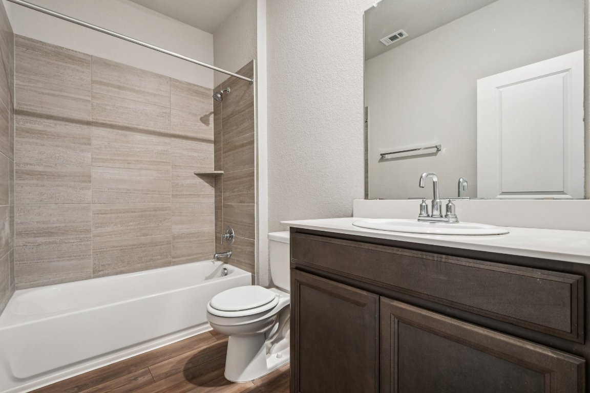 1007 Guadalupe Bass Road Hutto, TX 78634 - Photo 14 of 39 Bathroom with a textured wall, dark wood finished floors, bathing tub / shower combination, and vanity