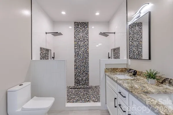 a bathroom with a granite countertop sink a toilet a mirror and shower