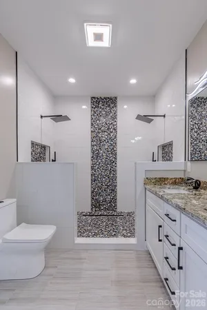 a bathroom with a granite countertop sink a toilet a mirror and shower