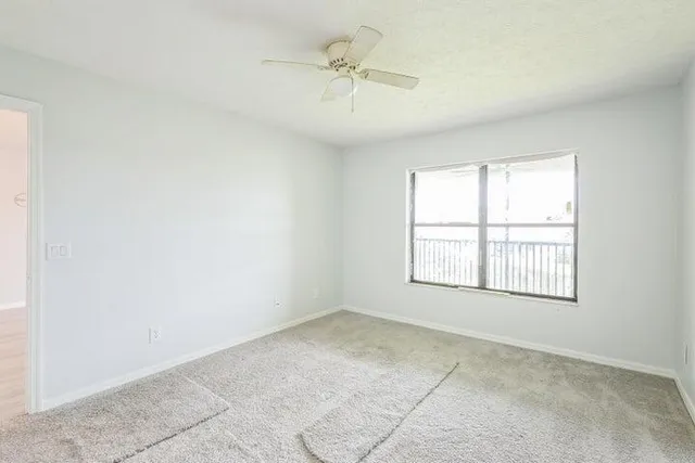 an empty room with chandelier fan and windows