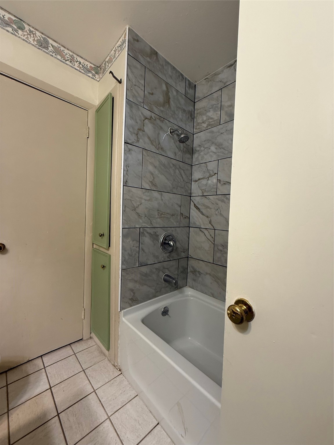 8140 Fondren Road, Unit 8140 Houston, TX 77074 - Photo 11 of 28 This bathroom features a bathtub with modern gray tile surround, a white tiled floor, and a small built-in cabinet for storage.