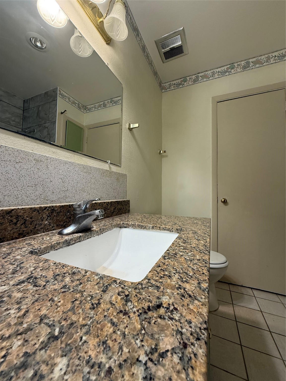 8140 Fondren Road, Unit 8140 Houston, TX 77074 - Photo 12 of 28 features a granite countertop with an undermount sink, a large mirror, overhead lighting, and a tiled floor. Subtle floral wallpaper adds a decorative touch.