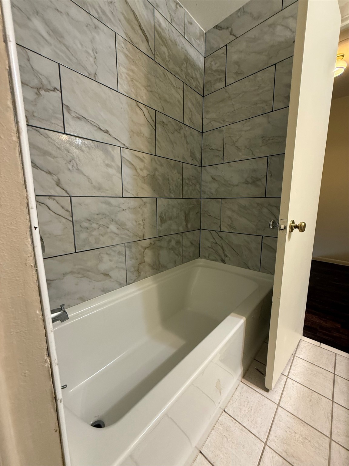 8140 Fondren Road, Unit 8140 Houston, TX 77074 - Photo 9 of 28 white bathtub with surrounding gray marble-patterned tiles, offering a clean and modern look.
