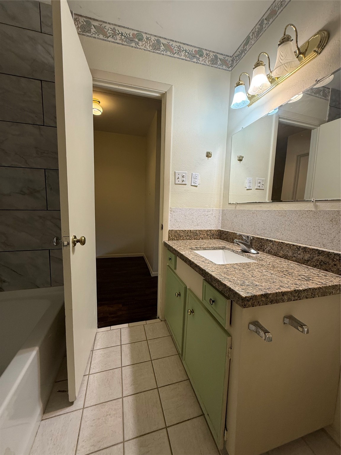 8140 Fondren Road, Unit 8140 Houston, TX 77074 - Photo 10 of 28 bathroom features a granite countertop with a single sink, under-cabinet storage, and a large mirror with overhead lighting. It has tiled flooring and a partially visible bathtub with a tiled wall. The space is bright and functional.