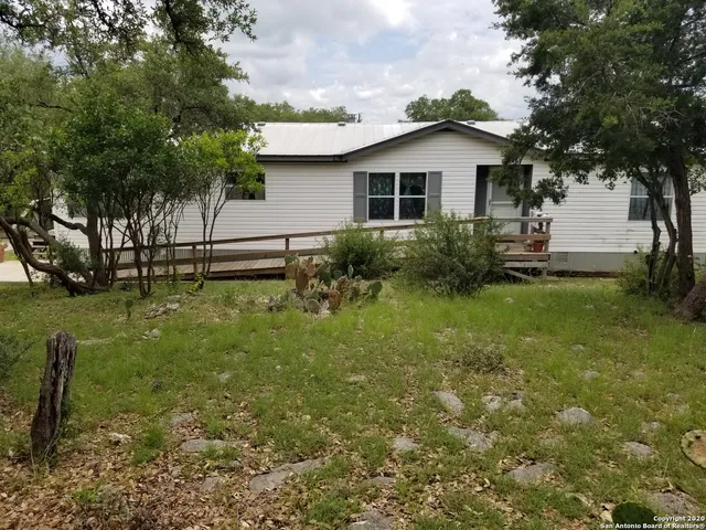 a backyard of a white house with potted plants and large trees