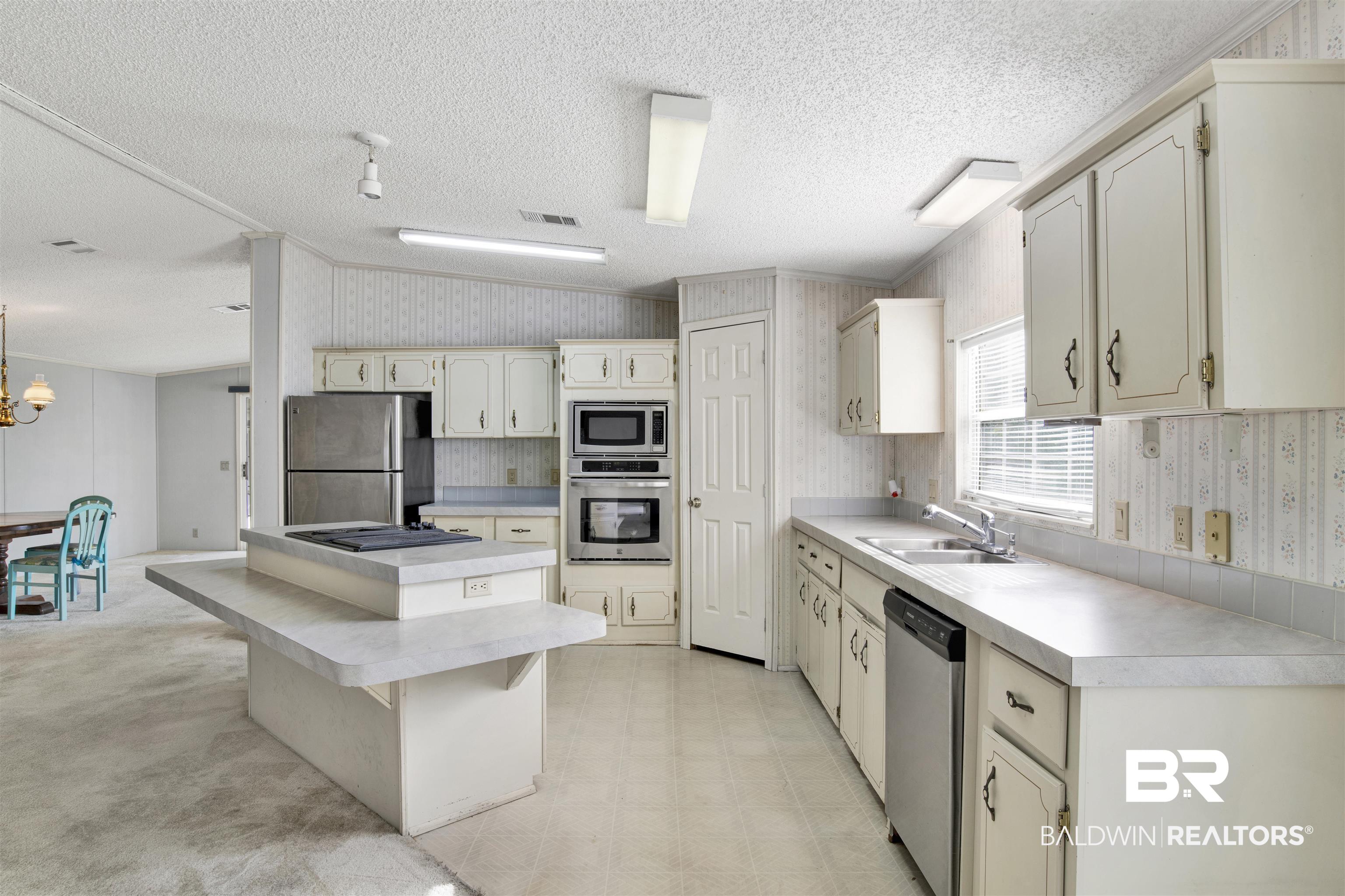 1216 Ridgewood Drive Lillian, AL 36549 - Photo 6 of 29 Kitchen with wallpapered walls, light countertops, a center island, a breakfast bar area, and appliances with stainless steel finishes
