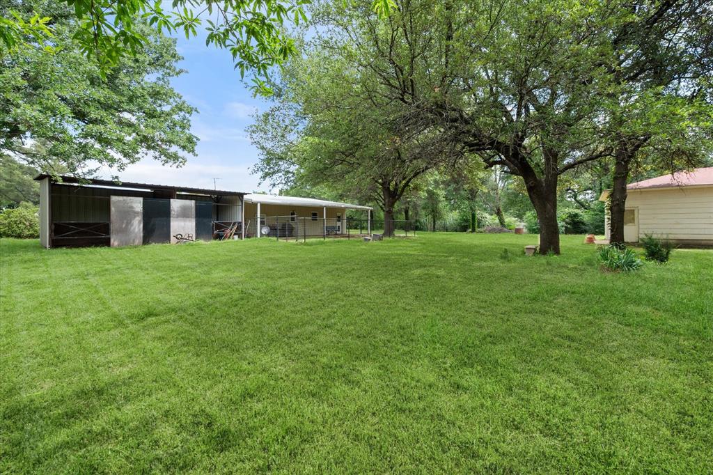126 Smallwood Court Springtown, TX 76082 - Photo 3 of 24 Two Stall Horse Barn, expansive green lawn featuring mature trees, a metal-roofed outbuilding/barn, and a covered patio area
