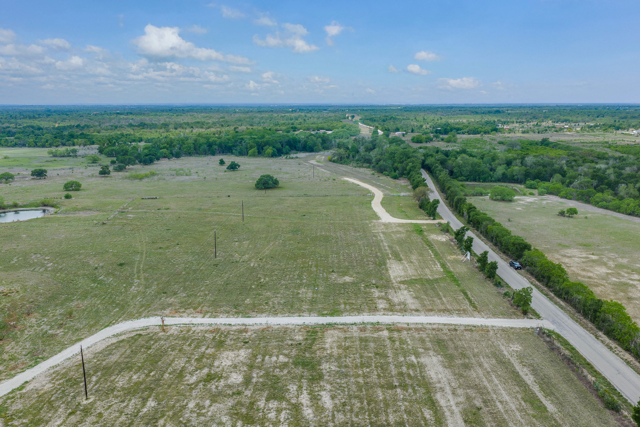 Lot 16 Mineral Springs Road Lockhart, TX 78644 - Photo 1 of 7 Expansive undeveloped land featuring a gravel road, paved road frontage, and a water feature
