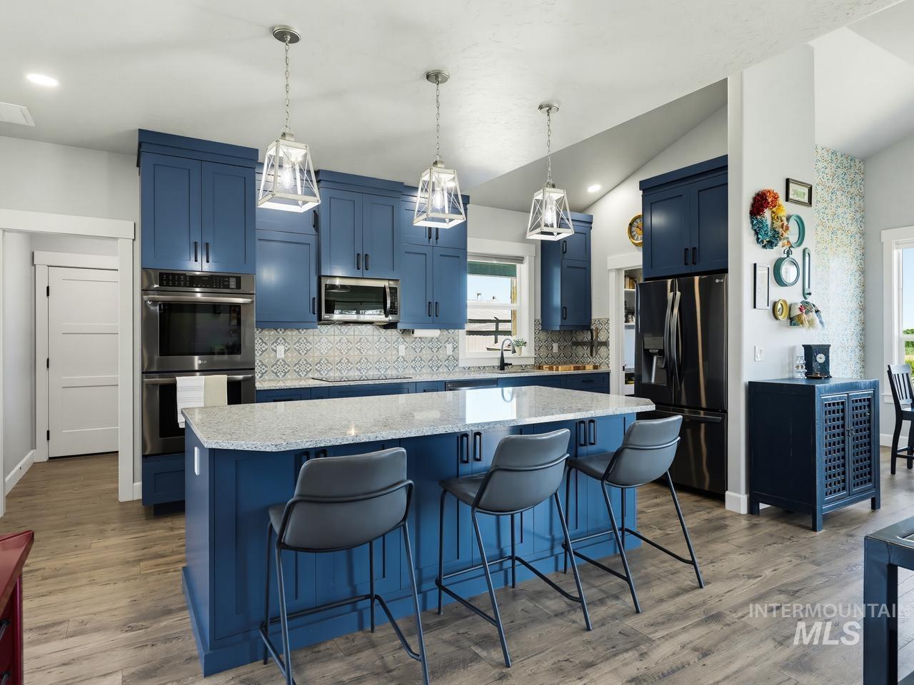 4950 West Columbia Road Nampa, ID 83687 - Photo 12 of 50 Kitchen featuring a central island with a light-toned countertop, blue cabinetry, stainless steel appliances, patterned backsplash, and wood-finish flooring