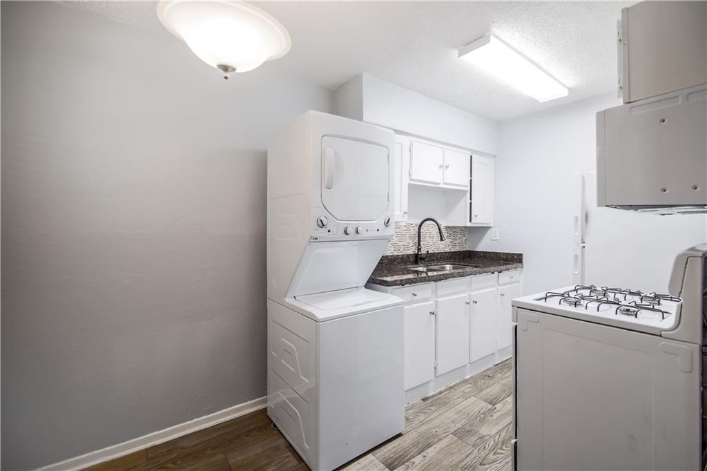 2401 Manor Road, Unit 102 Austin, TX 78722 - Photo 14 of 22 Kitchen featuring white gas range, white cabinets, light wood-style flooring, stacked washing machine and dryer, and a textured ceiling