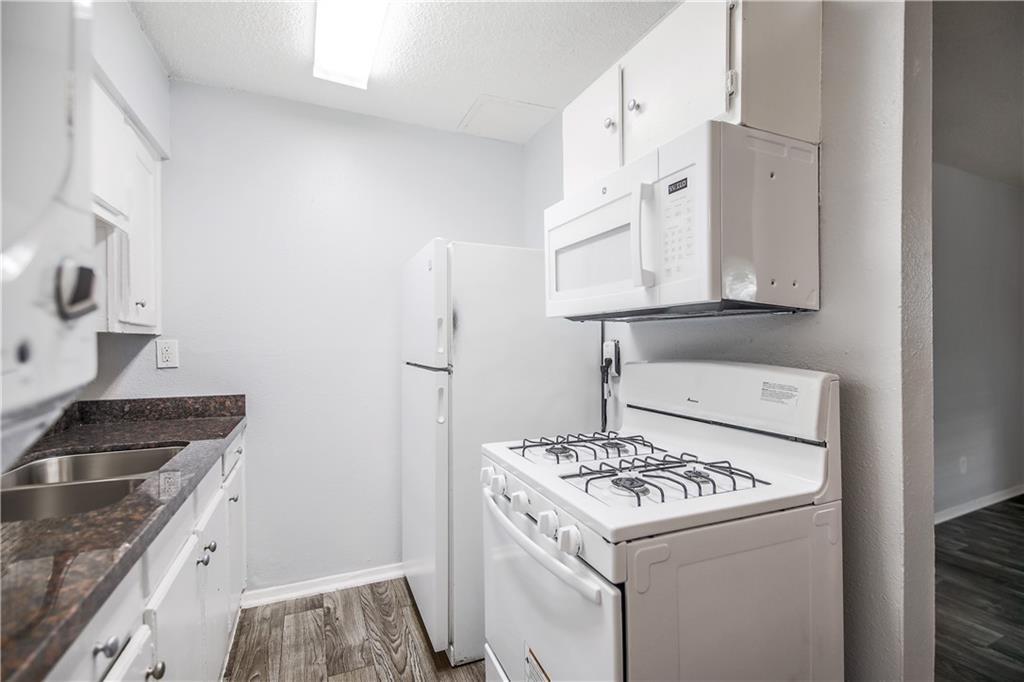 2401 Manor Road, Unit 102 Austin, TX 78722 - Photo 17 of 22 Kitchen with white appliances, white cabinetry, dark wood-style flooring, and a textured ceiling