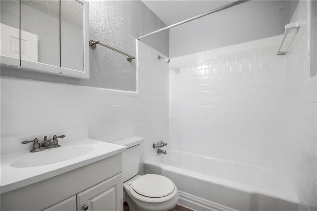 2401 Manor Road, Unit 102 Austin, TX 78722 - Photo 22 of 22 Full bath with vanity, shower combination, a textured wall, tile walls, and wainscoting