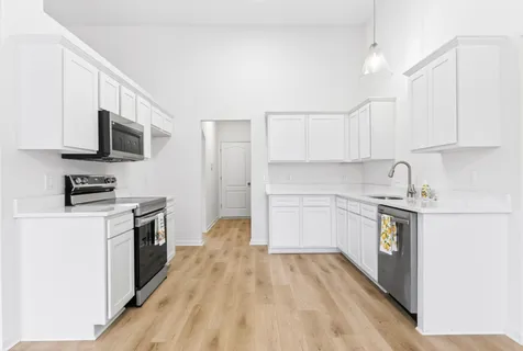 a kitchen with stainless steel appliances a stove top oven a sink a refrigerator white cabinets and wooden floor