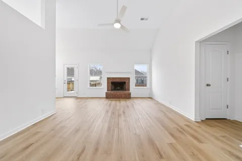 an empty room with wooden floor fireplace and windows