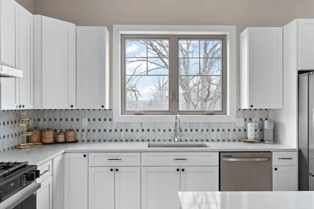 a bathroom with white cabinets sink and large window