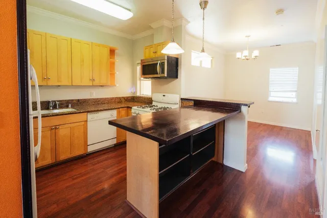 a kitchen that has a sink a microwave oven a stove white cabinetry and wooden floor